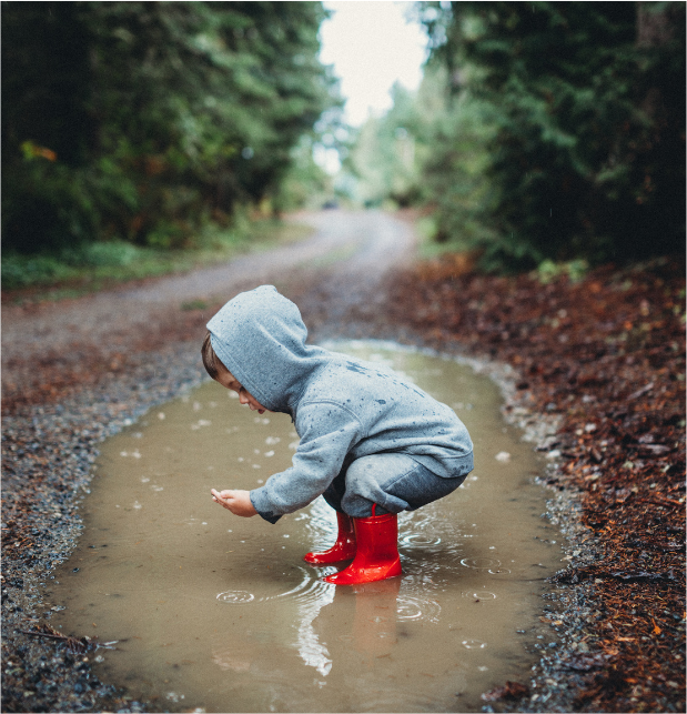 Boy jumping in a puddle outdoors showing the joy of messy, sensory play in nature