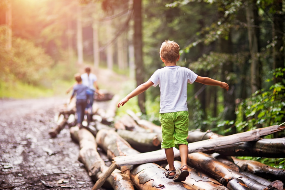 Two boys balancing on logs in nature showing the benefits of outdoor adventure play