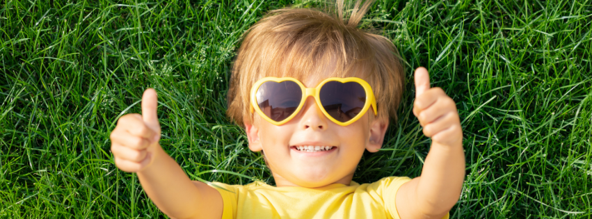 Boy lying on green grass outdoors representing the freedom and joy of natural play spaces